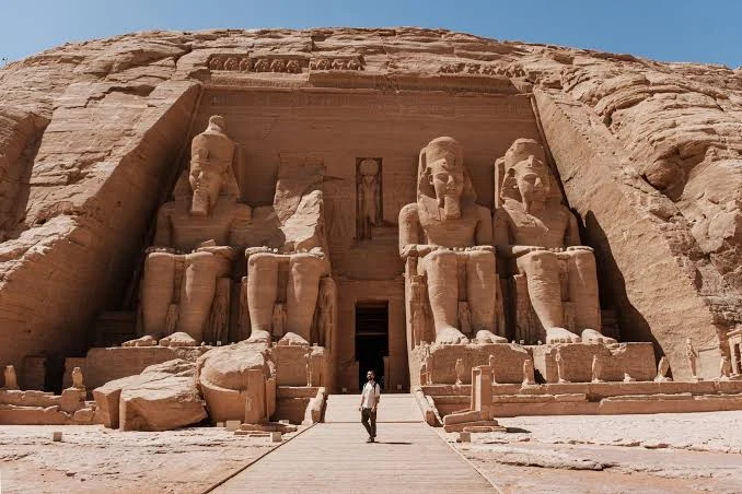 l'imponente facciata del Grande Tempio di Ramses II ad Abu Simbel, scolpita in una parete di roccia. La facciata è dominata da quattro colossali statue sedute del faraone Ramses II, ciascuna alta circa 20 metri, scolpite con dettagli intricati nel arenaria